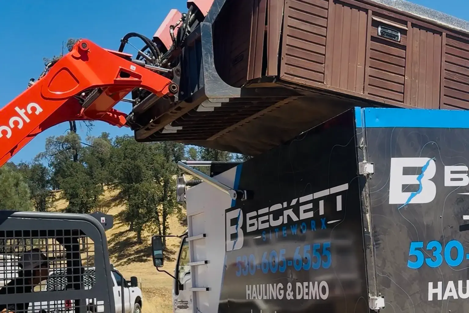Excavator loading a hot tub into a hauling truck for removal