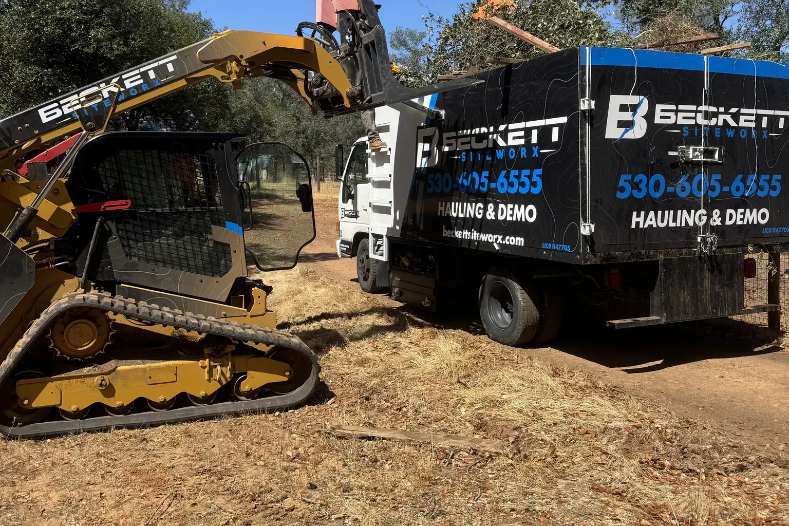 Track loader loading brush and yard waste into hauling truck
