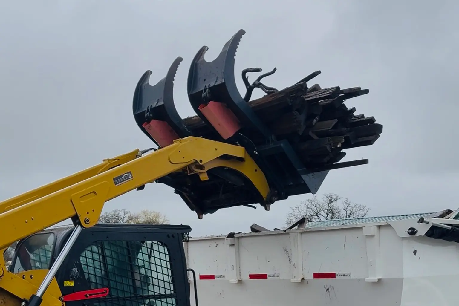 Track loader loading commercial junk into dump trailer
